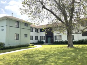 Exterior view of building 4136 at a well-maintained apartment complex, featuring two stories, black-trimmed windows, and a manicured lawn with mature tree and pathway.