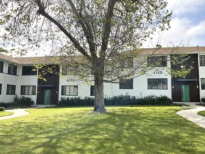 Front view of buildings 4135 and 4140 in a garden-style apartment community, showcasing clean white facades, green entry doors, and shared green space with mature landscaping.
