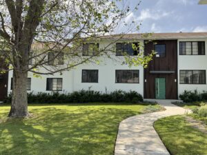 Direct view of building 4141's entrance with green accent door and brown wood paneling, surrounded by low shrubs and a curved sidewalk leading through a grassy courtyard.
