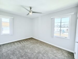 Interior Unit Bedroom, Neutral toned carpeting, White walls, Multiple windows in bedroom, ceiling fan/ light.