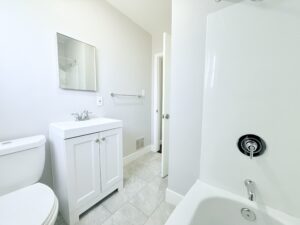Interior Unit bathroom, white walls, white tile floor, white vanity, shower/bath.