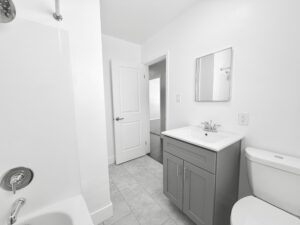Interior Unit Bathroom, white walls, white bathroom sink with gray vanity, shower/bath, stone tile floor.
