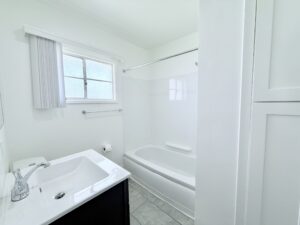 Interior Unit Bathroom, white walls, white bathroom sink with gray vanity, shower/bath, stone tile floor.
