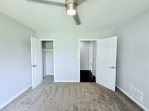 Interior Unit Bedroom, neutral toned carpeting in bedroom, neutral toned walls, wood floors in hallway, Ceiling fan.