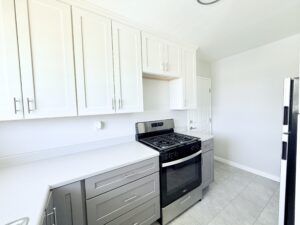 Interior Unit Kitchen, Stone tile floor, white and gray cabinetry, stainless steel appliance, white walls.