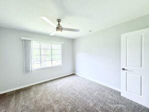 Interior Unit Bedroom, neutral toned carpeting in bedroom, neutral toned walls, wood floors in hallway, Ceiling fan.