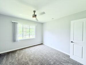 Interior Unit Bedroom, neutral toned carpeting in bedroom, neutral toned walls, wood floors in hallway, Ceiling fan.