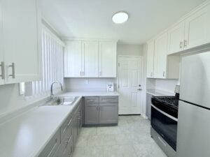 Interior Unit Kitchen, Stone tile floor, white and light gray cabinetry, stainless steel sink, stainless steel appliances, vinyl countertop.